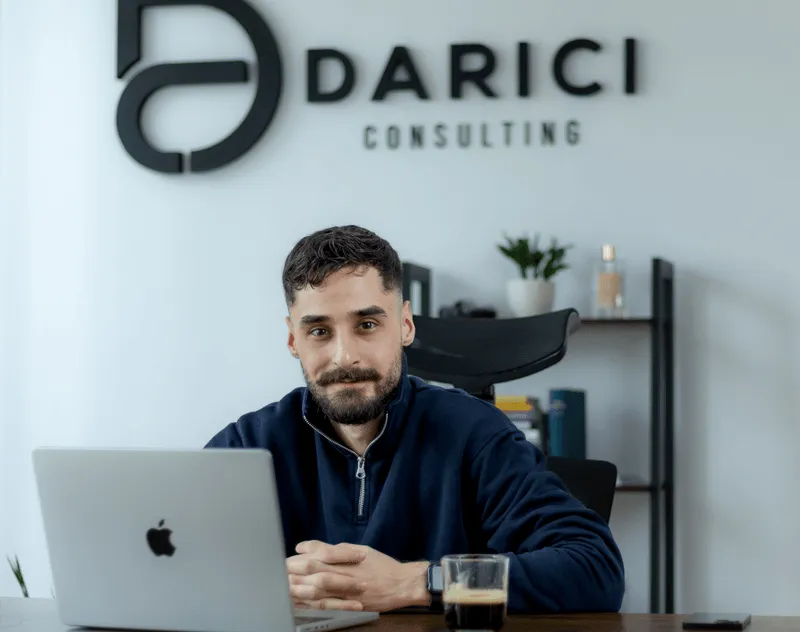 Gökhan Darici am Schreibtisch vor dem Darici-Consulting-Logo